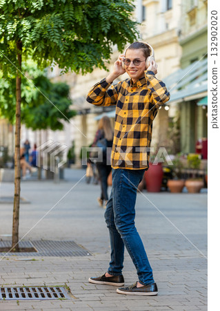 Rear view of happy relaxed man tourist in wireless headphones listening music walking on city street 132902020