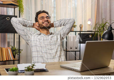 Indian businessman working on laptop putting on earbuds listening music taking a break relaxing 132902053
