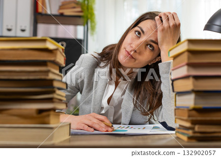 Exhausted business woman looking at documents reports stacks of books while working hard at office 132902057