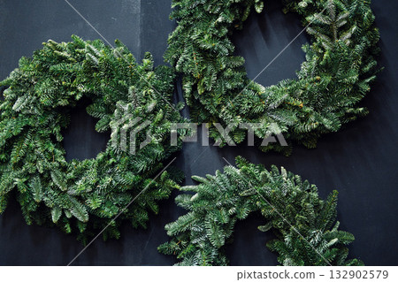 Three handmade evergreen wreaths arranged on a dark surface. Holiday crafting kits, personalized festive decor, seasonal product diversity, consumer co-creation Three handmade evergreen wreaths arranged on a dark surface. Holiday crafting kits, personalized festive decor, seasonal product diversity, consumer co-creation 132902579
