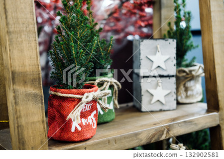 Mini Christmas trees in colorful fabric pots sit on a wooden shelf decorated with stars. Sustainable holiday decor, zero waste gifting, eco-friendly living, rustic interior design Mini Christmas trees in colorful fabric pots sit on a wooden shelf decorated with stars. Sustainable holiday decor, zero waste gifting, eco-friendly living, rustic interior design 132902581