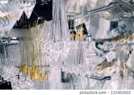 Close-up of faceted crystal ornaments with gold hanging threads displayed in a holiday retail setting. Gemstone Christmas trends, metallic threads, fine-detail festive products 132902602