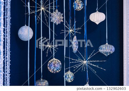 Hanging crystal and glass Christmas ornaments with starburst lights on a dark blue backdrop. Iridescent ornaments, celestial holiday trend, crystal starburst lights, cosmic Christmas 132902603