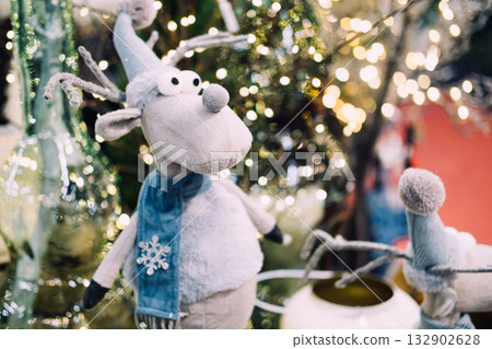 A soft plush reindeer toy with a long striped hat and googly eyes set against a background of Christmas lights. Quirky Christmas decor, playful reindeer toy, whimsical holiday trends A soft plush reindeer toy with a long striped hat and googly eyes set against a background of Christmas lights. Quirky Christmas decor, playful reindeer toy, whimsical holiday trends 132902628