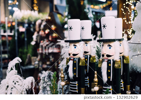 Wooden nutcracker soldier decorations in a Christmas market surrounded by lights, trees, and holiday decor. Christmas nostalgia, nutcracker tradition, vintage holiday decor, festive folklore Wooden nutcracker soldier decorations in a Christmas market surrounded by lights, trees, and holiday decor. Christmas nostalgia, nutcracker tradition, vintage holiday decor, festive folklore 132902629