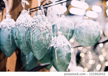 Close-up of icy blue Christmas ornaments with glitter and snow-like texture hanging on display. Christmas ornament design, holiday sparkle aesthetics, winter luxe decor, festive retail presentation 132902632