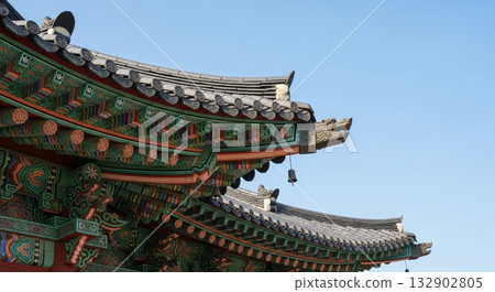Traditional Korean temple roof architecture with colorful dancheong painted wooden brackets and curved gray tile eaves against clear blue sky 132902805
