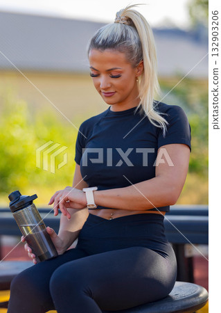 Woman in athletic attire using smartwatch during outdoor workout session Woman in athletic attire using smartwatch during outdoor workout session 132903206