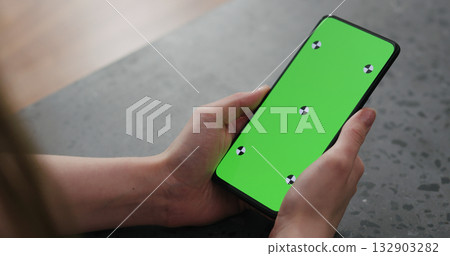 Young woman sitting at a counter and using smartphone with green screen Young woman sitting at a counter and using smartphone with green screen 132903282