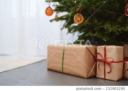 Small christmas tree with gifts in paper wrap near window 132903290
