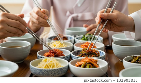 Asian hands using metal chopsticks sharing traditional Korean banchan side dishes from ceramic bowls during family meal 132903813
