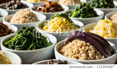Traditional Korean banchan side dishes in white ceramic bowls featuring seasoned spinach, bean sprouts, eggplant slices, and various fermented vegetables arranged for authentic Korean meal service 132903867