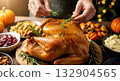 Hands garnishing a roasted turkey with rosemary sprigs, surrounded by Thanksgiving side dishes and pumpkins. 132904565