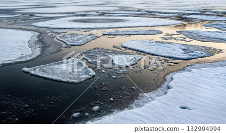 Partially Frozen Lake with Floating Ice Sheets Creating Abstract White and Black Pattern and Water Reflection 132904994