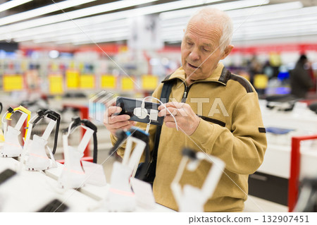 elderly man examines tablet computer in showroom of electronics store elderly man examines tablet computer in showroom of electronics store 132907451