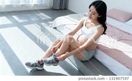 pregnant woman tying shoelaces on bed edge, calm morning light, intimate focused moment at home 132907597
