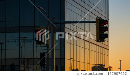 Traffic light embedded in mirrored building facade with sunset reflections and city lights below 132907612