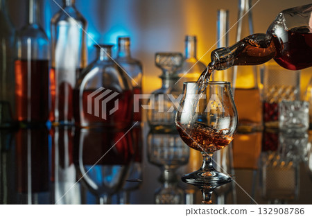 Brandy is poured from a bottle into a glass. Brandy is poured from a bottle into a glass. 132908786