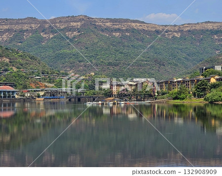 Hill town reflection Scenic hillside town reflected in calm lake water under clear skies, showing harmony between architecture and nature. 132908909