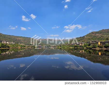 Mirror lake landscape Crystal-clear lake reflecting surrounding hills and blue sky, representing tranquility, balance, and pristine nature. 132908910