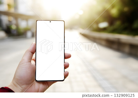 A person holds a blank screen smartphone outdoors in the sunlight. 132909125