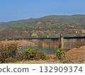 Mountain dam landscape Wide view of a dam surrounded by green hills and dry vegetation under bright sunlight, capturing natural engineering amidst rugged terrain. 132909374