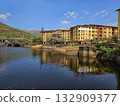Colorful lakeside town Brightly painted buildings reflecting on a calm lake surrounded by green hills, capturing vibrant urban beauty amid nature. 132909377