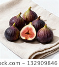 Group of ripe figs arranged on a folded neutral cloth, one cut open to reveal its deep red interior and soft texture.  132909846