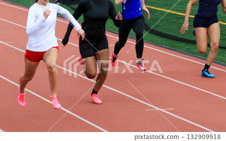 Four Female Runners Sprinting on Track During a Competitive Race Event 132909918
