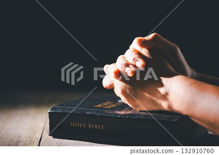 Hands clasped in prayer over the holy Bible, the faithful Christian worships God in church, holding onto hope and belief, guided by religion and a deep commitment to their religious faith. 132910760