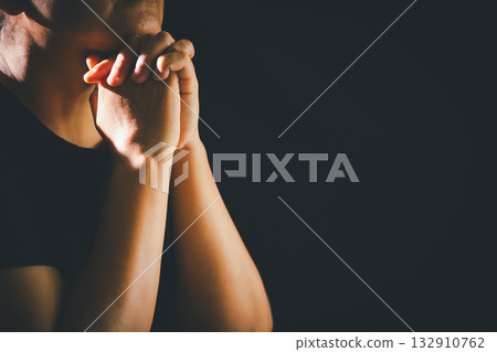 Dark silence of the church, a Christian lifts their hand in prayer to God, a symbol of worship, faith, and hope-embracing the spiritual concept of religion and believing in Jesus Christ. 132910762