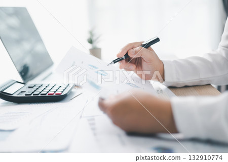 A businesswoman reviews financial report while holding documents and pointing with pen at office desk. Concept of accounting, budget management, financial analysis and corporate business planning. 132910774