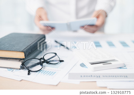 A businesswoman analyzes financial charts and reports with pen while reviewing documents on clipboard at office desk. Concept of accounting, business planning, data analysis and corporate strategy. A businesswoman analyzes financial charts and reports with pen while reviewing documents on clipboard at office desk. Concept of accounting, business planning, data analysis and corporate strategy. 132910775