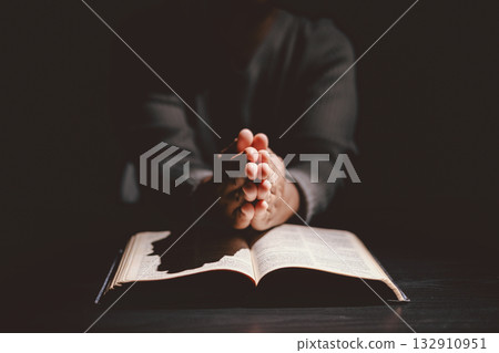 Hands folded in prayer on the Holy Bible, symbolizing faith, devotion, Christianity, hope, and spiritual strength. Concept of worship, meditation and trusting God Word. 132910951