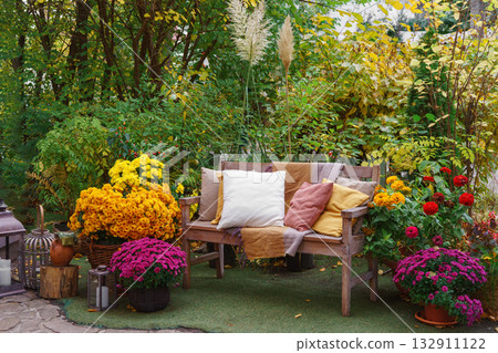 Wooden garden bench with pillows among autumn flowers and colorful foliage in fall backyard 132911122