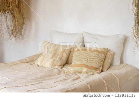 Soft beige pillows, decorative cushions on cozy bed with natural linen textile in bright sunlight 132911132