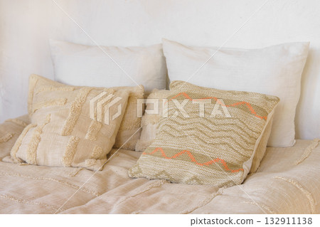 Soft beige pillows, decorative cushions on cozy bed with natural linen textile in bright sunlight 132911138