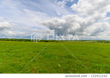 A Vast Green Meadow Spreading Across the Landscape Under a Dramatic Cloudy Sky Above 132911242