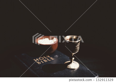 Holy communion bread and wine cup placed on the Holy Bible, symbolizing the Lord Supper, Eucharist, sacrifice of Jesus Christ, Christian worship and remembrance of faith. Holy communion bread and wine cup placed on the Holy Bible, symbolizing the Lord Supper, Eucharist, sacrifice of Jesus Christ, Christian worship and remembrance of faith. 132911329