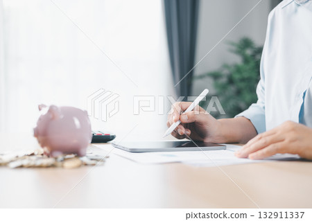 Concept of saving money and financial security. Pink piggy bank surrounded by coins on office desk with businesswoman in background, symbolizing investment, wealth growth and budget management. Concept of saving money and financial security. Pink piggy bank surrounded by coins on office desk with businesswoman in background, symbolizing investment, wealth growth and budget management. 132911337