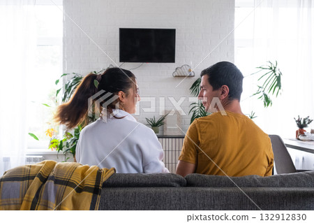 Man and woman at home in a white interior sits on the couch and watches TV, black screen mock up. Home recreation, leisure, love, family, date Man and woman at home in a white interior sits on the couch and watches TV, black screen mock up. Home recreation, leisure, love, family, date 132912830