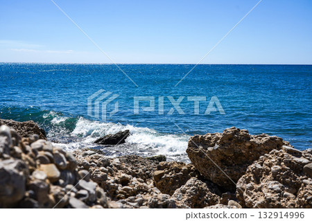 A Serene Coastal View with Clear Blue Waters and Rocky Shoreline Under Bright Sunshine on a Perfect Day 132914996