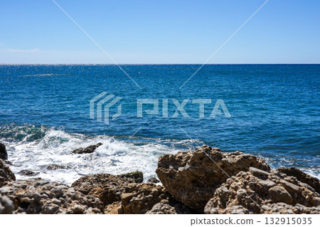 A Tranquil Coastal Scene with Lapping Waves Against Rocky Shoreline Under Clear Blue Skies Reflecting the Beauty of Nature's Harmony A Tranquil Coastal Scene with Lapping Waves Against Rocky Shoreline Under Clear Blue Skies Reflecting the Beauty of Nature's Harmony 132915035