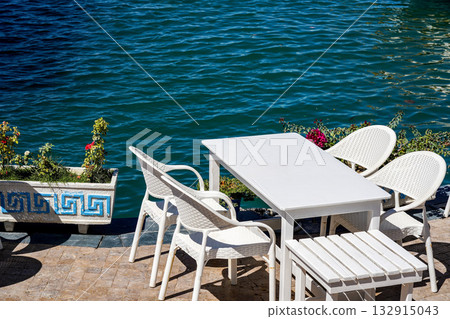 A Tranquil Waterfront Scene Featuring White Furniture and Calm Waters Surrounded by Lush Greenery and Colorful Flowers A Tranquil Waterfront Scene Featuring White Furniture and Calm Waters Surrounded by Lush Greenery and Colorful Flowers 132915043