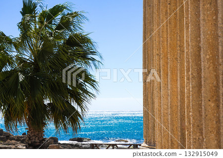 A Scenic View of Ancient Columns and Lush Palm Trees Overlooking a Tranquil Ocean Under a Bright Blue Sky A Scenic View of Ancient Columns and Lush Palm Trees Overlooking a Tranquil Ocean Under a Bright Blue Sky 132915049