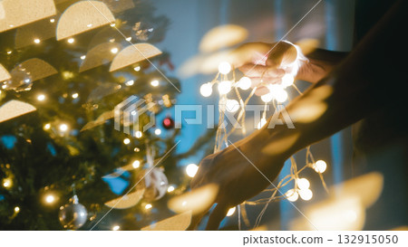 Man twisting Christmas lights in a night room 132915050