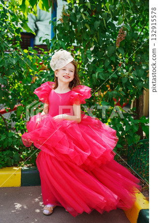 A girl in a lush pink dress and hat near the green bushes A girl in a lush pink dress and hat near the green bushes 132915578