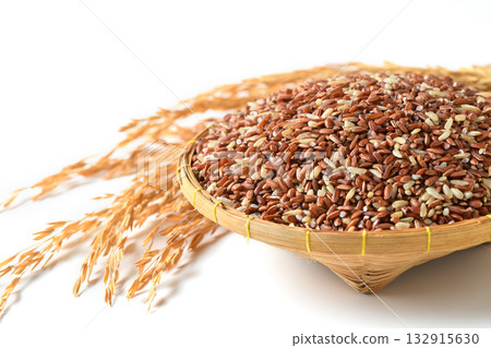 Close up of organic brown rice grains in a bamboo basket with golden rice stalks on a white background. Close up of organic brown rice grains in a bamboo basket with golden rice stalks on a white background. 132915630