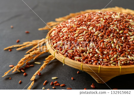 Close up of organic brown rice grains in a bamboo basket with golden rice stalks on black stone background. Close up of organic brown rice grains in a bamboo basket with golden rice stalks on black stone background. 132915662