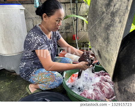 An Asian woman washes clothes by hand in a basin An Asian woman washes clothes by hand in a basin 132915723